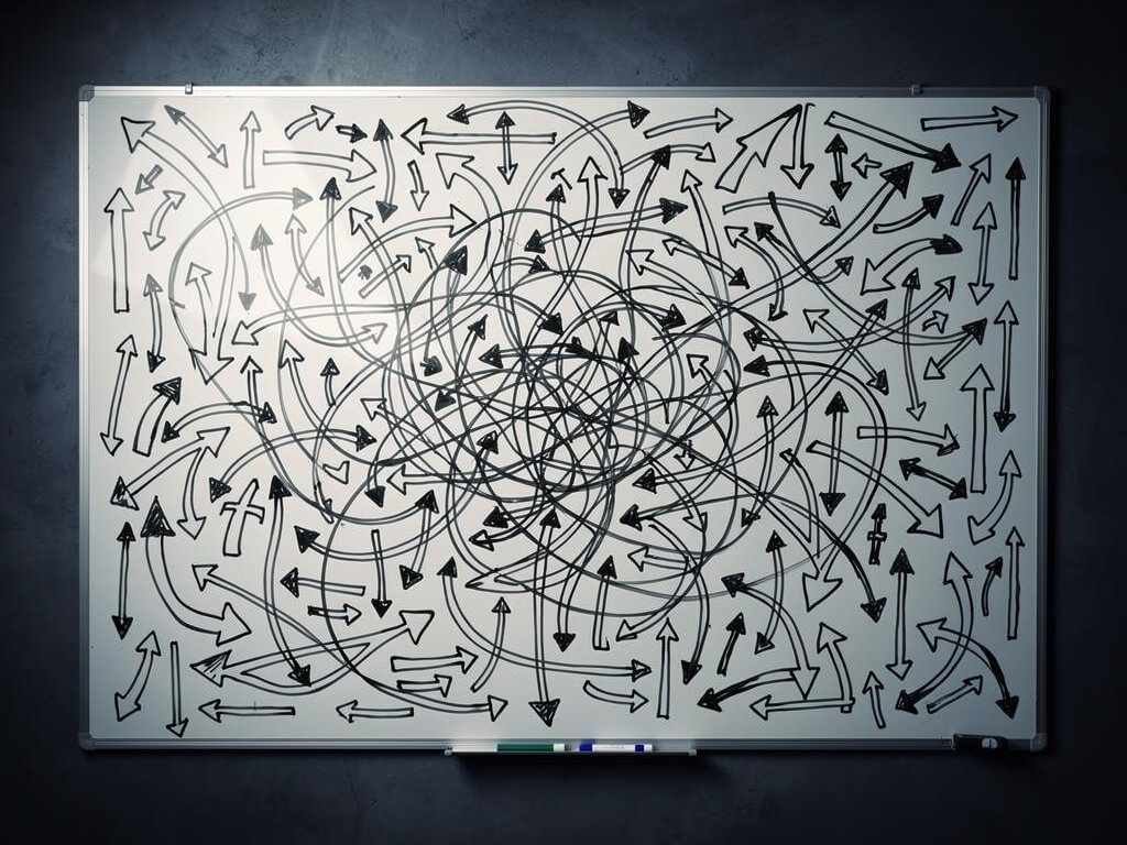 Whiteboard completely covered in hundreds of arrows pointing in every direction, crossing and overlapping, some circling back on themselves, chaotic indecision visualization, dark background, overhead view