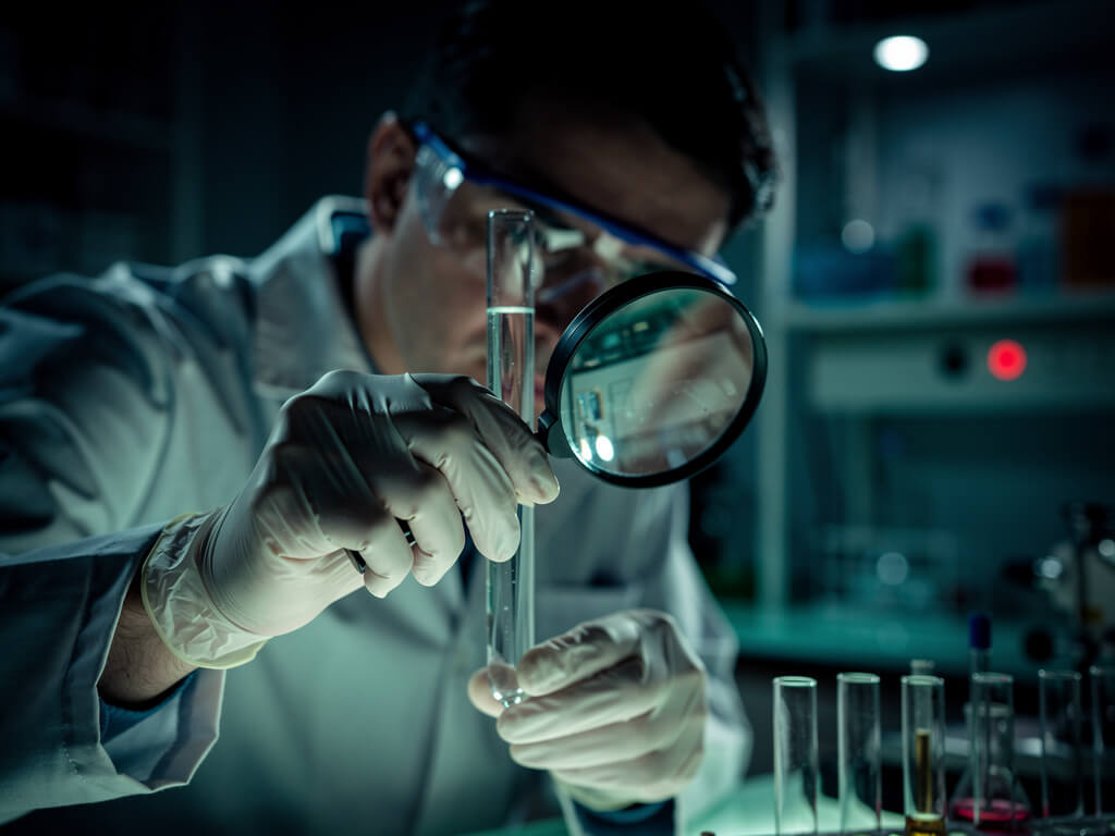 Scientist carefully examining a test tube under a magnifying glass, methodical and precise, lab equipment in background, dark moody lighting, shallow depth of field