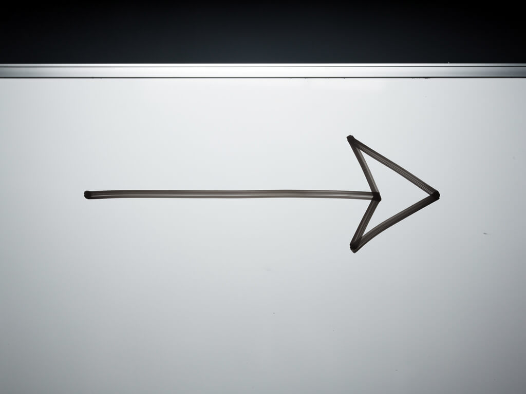 Single straight arrow drawn on a clean whiteboard pointing clearly to the right, minimal and decisive, dark background, calm and confident composition, studio lighting