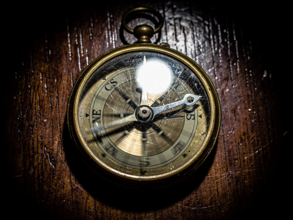 Vintage compass with the needle spinning wildly in multiple directions at once, motion blur on the needle, dark wooden surface, dramatic overhead lighting, macro photography